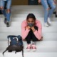 2021 national school climate survey: young black student with facemask sitting on steps sadly while other students walk by