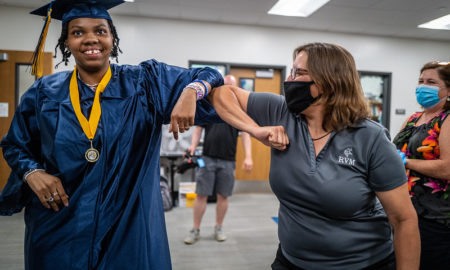 disabled people legal guardianship: Black woman with short braids in blue graduation robe and cap bumps elbows with woman wearing mask and grey t-shirt