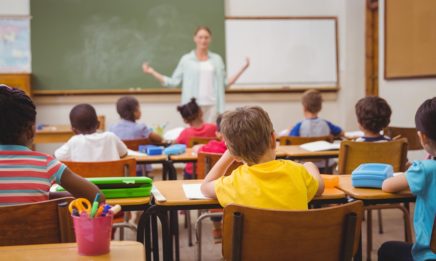 full-service community schools report: view of classroom from behind students as teacher teachers