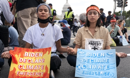 Youth climate activists: Two teen girls inforeground of crownd sitting in the street holding signs abut climate change