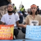 Youth climate activists: Two teen girls inforeground of crownd sitting in the street holding signs abut climate change