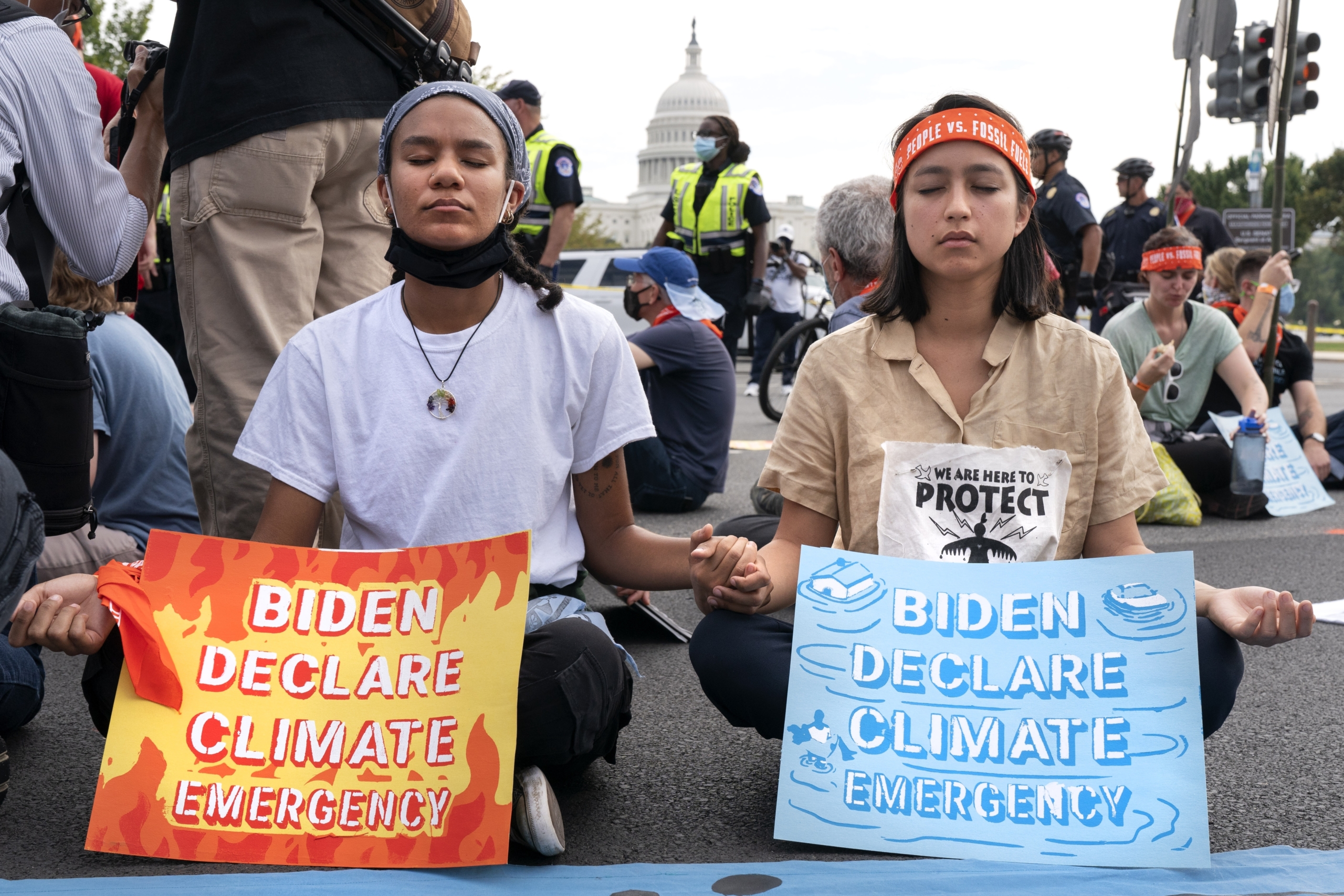 Youth climate activists: Two teen girls inforeground of crownd sitting in the street holding signs abut climate change