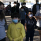 Afterschool funding: Parents & children wearing masks standing in line outside.