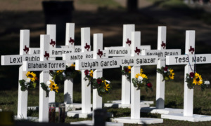 School shootings: White crossed with names in black paint and flowers on them in grassy area