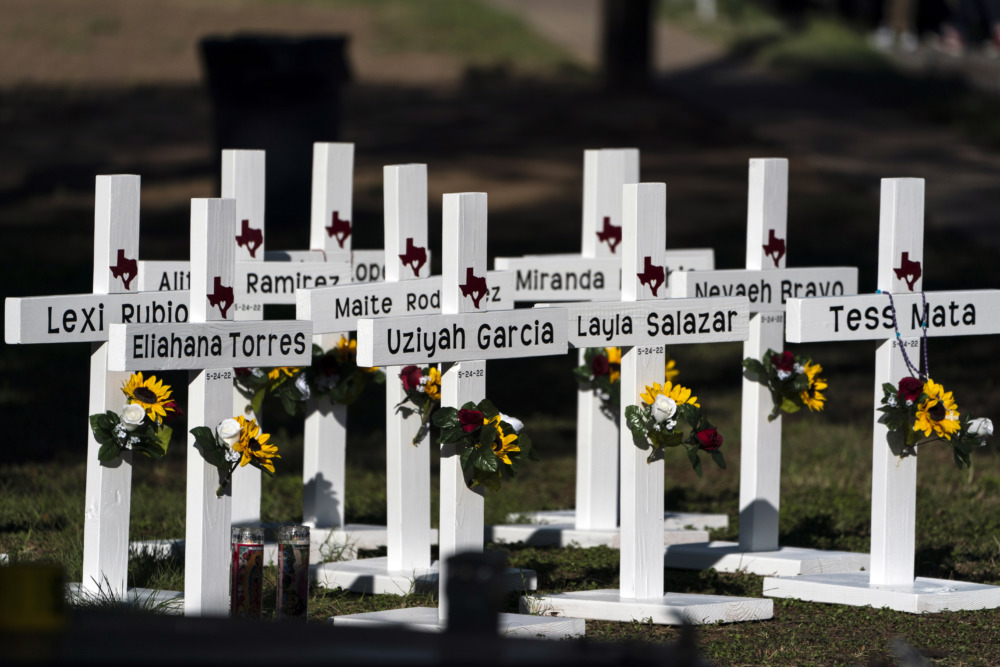 School shootings: White crossed with names in black paint and flowers on them in grassy area