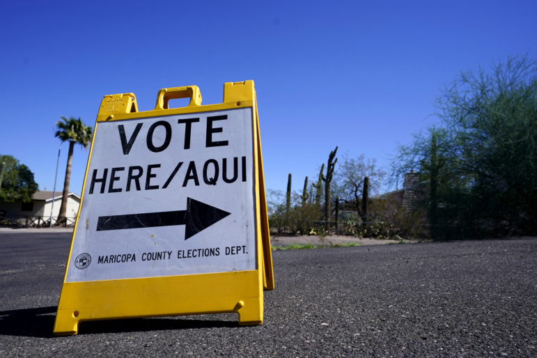 Youth climate activists: Yellow sandwich sign on asphalt with white sign that says Vote here/aqua and a black arrow