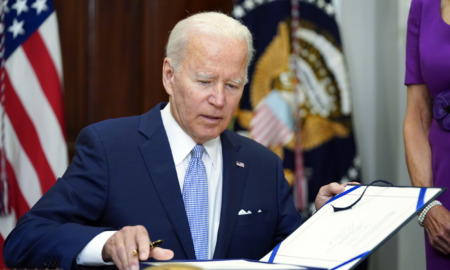 gun safety bill: President Biden, white-haired man in navy suit, white shirt and light blue tie, sidns page in large, open cook.