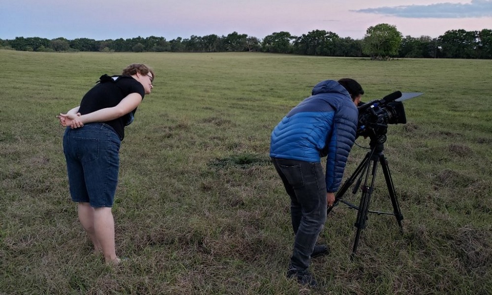 Being Michelle documentary: two people stand in a field with one in jacket looking through camera on tripod 