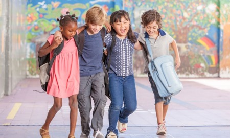 education equity, child/youth conflict resolution and resiliency grants: group of four diverse children with backpacks hugging while walking