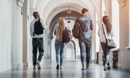 colleges are closing at pace of one a week: four college students walking down campus hallway away from camera