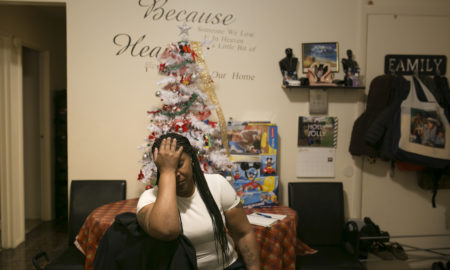 Woman in white top holds hand to forehead in front of white tabletop Christmas tree.