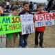 March for Our Lives: 3 boys hold up their signs; one in glasses and tan pants; one in dark jacket and jeans; one in red jacket and dark jeans.