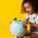 child development, early childhood grants: young girl looking at globe with yellow background