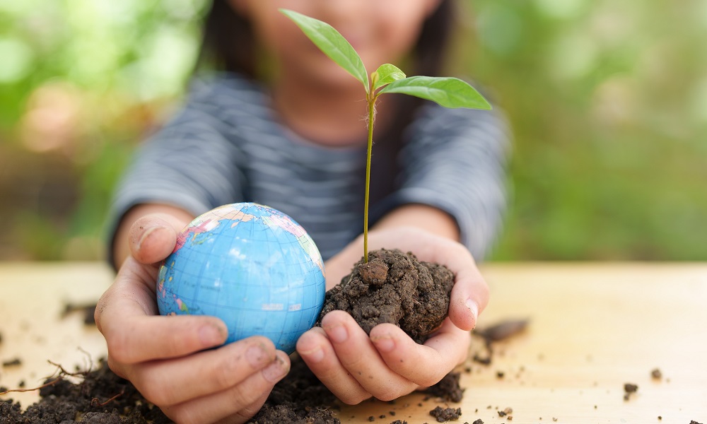 Youth-led project, environmental education grants: little girl holding globe and newly sprouted tree in soil