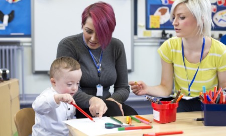 early education for children with disabilities: two teachers help a young child with down syndrome paint