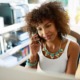 Black women-owned business support grants; young black businesswoman chatting on a mobile phone to a client as she sits working in a bright airy office