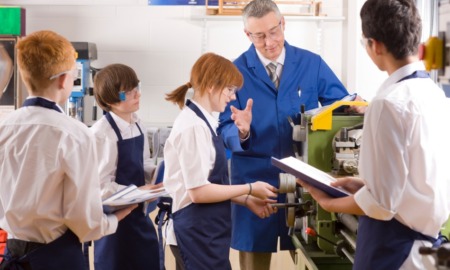 High school skilled trades education educator award grants: Teacher demonstrating lathe to high school pupils in metalwork class