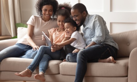 family economic mobility and healthy homes grants: young black family on couch laughing while looking at tablet device