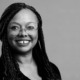 Holly Whitfield headshot: black woman with glasses and long hair in front of gray background