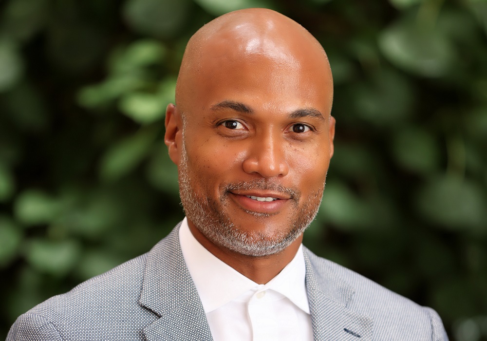 Jermaine Myrie named CEO of MENTOR: black, bald man with greying short beard wearing suit in front of out-of-focus plant backdrop