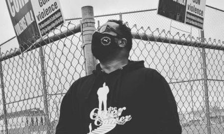 Gun violence survivors in separate cities: man in black hoodie and glasses in front of fence with gun violence signs on it