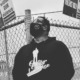 Gun violence survivors in separate cities: man in black hoodie and glasses in front of fence with gun violence signs on it