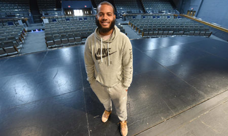 theater: Smiling young man in gray Nike sweats stands on theater stage.