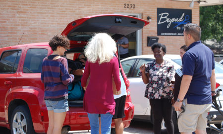 host homes: Group of people stand around opened trunk of minivan.