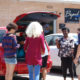 host homes: Group of people stand around opened trunk of minivan.