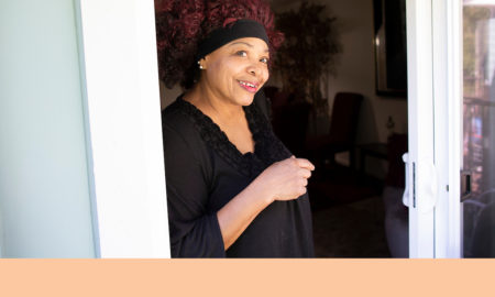 host home: Smiling woman with red hair held back by black hairband stands at door.