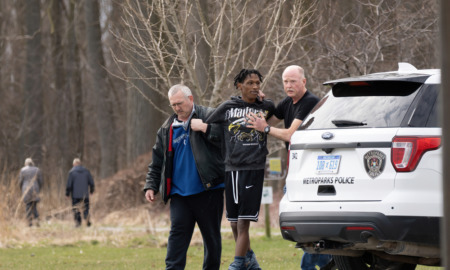 Juvenile Sentencing: Two policeman holding Black male teen between them walt around whote police car in a grassy park