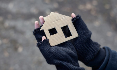 Partially gloved mittens holding a cardboard cutout of a house, with fuzzy background.