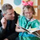 Positive Tomorrows: Beaming little girl holds open book as man on couch looks at it.