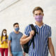 students not returning to school: young adultstudents lined up 6 feet apart wearing masks standing in front of cream brick wall