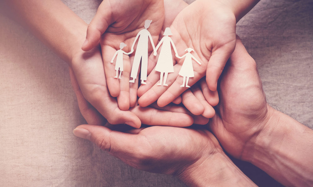 Therapeutic foster care, family unification: Hands palms up overlapping holding paper cutout of 2 adults with 2 children holding hands