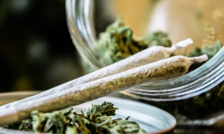 NY marijuana laws: Two hand-rolled marijuana joints rest on lid and glass jar lying on its side with marijuana buds in it