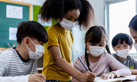 Student Masks Texas_4 youg students wearing masks gather around a paper prject they are working on together in a classroom