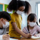 Student Masks Texas_4 youg students wearing masks gather around a paper prject they are working on together in a classroom