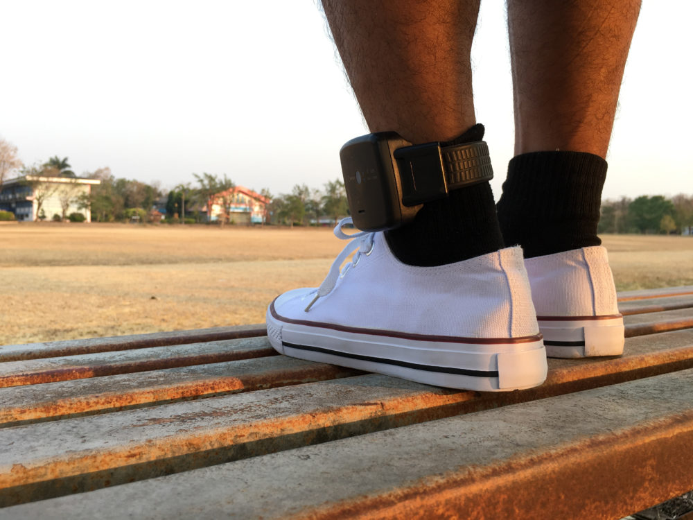 Juvenile diversion and probation: Closeup of two feet wearing white tennis shoes and black socks with an ankle monitor on left ankle