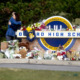 school shooting: Oxford high school sign covered in flowers and memorial items while two people hug