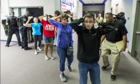 School shootings: Line of several teens with hands up behind heads stand in side building hallway