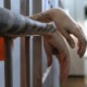 Girl vs. boy juvenile incarceration: A person's tattooed forearms and hands dangle between cell bars.