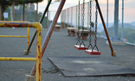 Child Abuse Reporting: Ols, rust playground swings on fenced, asphalt playground