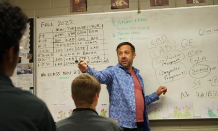 Utah College Classes: Man in blue shirt gestures speaking to clas stanng in front of a white board filled with text