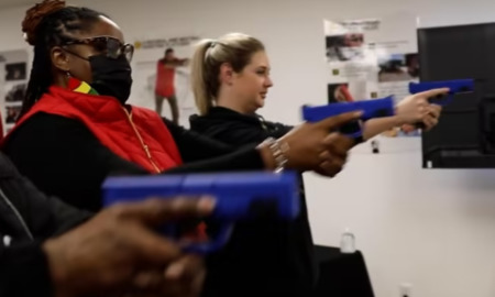 Female gun use: Two women aiming blue plastic handguns at targets during indoor training session