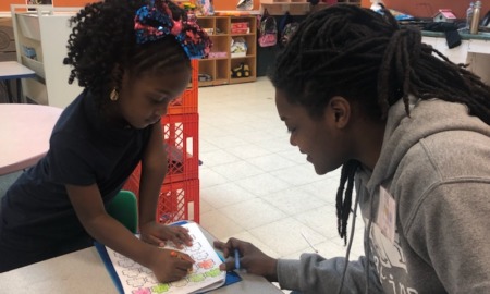 OST Staff: Woman and young child sit at low classroom ttabe working on art