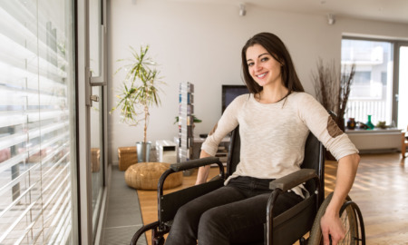 Reproductive Health Care: Dark-haired woman in ta shirt and vbrown pants sits in wheelchair in modern office waiting room