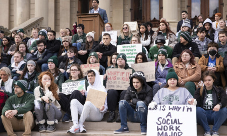 Michigan Gun Law: Group of dozens of adults with protest signs sit on wide cement steps to building entrance