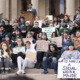 Michigan Gun Law: Group of dozens of adults with protest signs sit on wide cement steps to building entrance