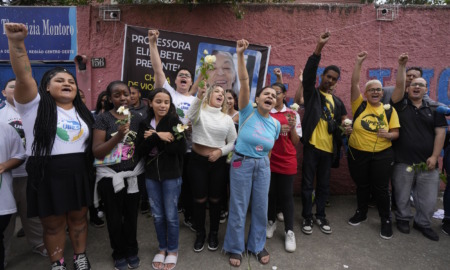 Brazil school violence: Middle school age children stand with fists raised and protest signs om front of red brick wall